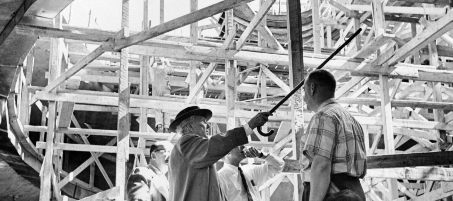 Frank Lloyd Wright standing at construction site of Guggenheim Museum wearing hat and pointing cane at scaffolding